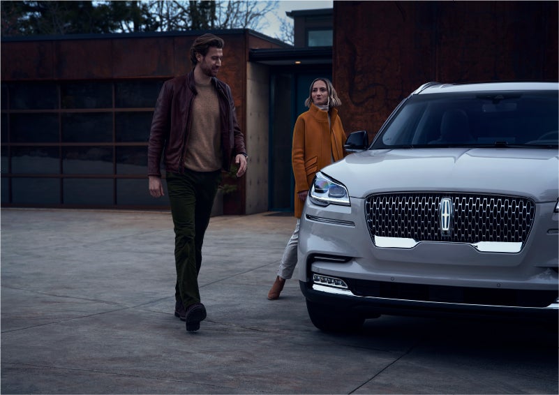 A man and a woman approaching a 2023 Lincoln Aviator® SUV, which illuminates certain lights when they are close | Gates Lincoln in Richmond KY