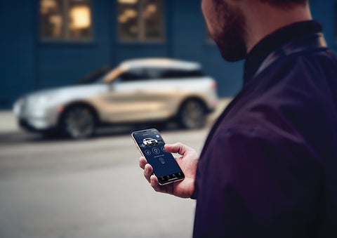 A person is shown interacting with a smartphone to connect to a Lincoln vehicle across the street. | Gates Lincoln in Richmond KY