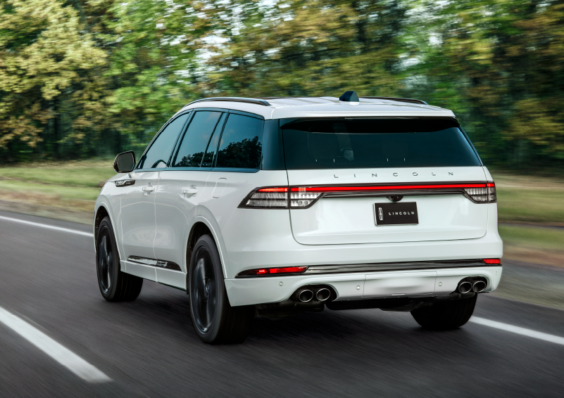 A white 2025 Lincoln Aviator® SUV is being driven away down a road lined with colorful trees. | Gates Lincoln in Richmond KY