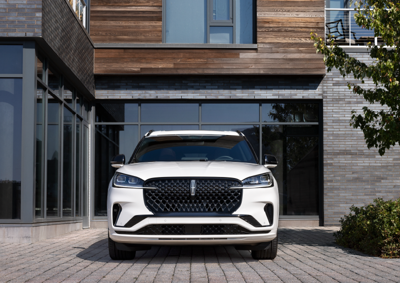 A white 2025 Lincoln Aviator® SUV is shown parked outside a modern building with gray brick and wood accents. | Gates Lincoln in Richmond KY