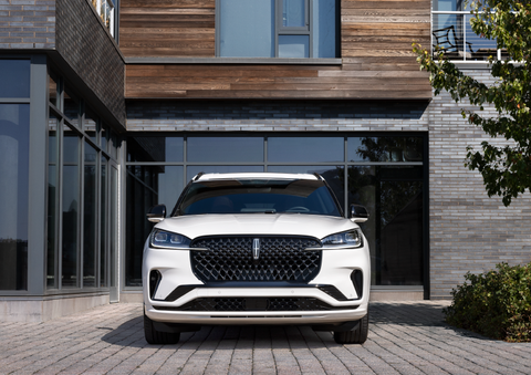 A white 2025 Lincoln Aviator® SUV is shown parked outside a modern building with gray brick and wood accents. | Gates Lincoln in Richmond KY