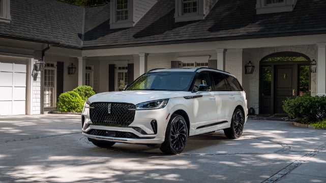 A white 2026 Lincoln Aviator® SUV is parked in the driveway of a luxury home. | Gates Lincoln in Richmond KY